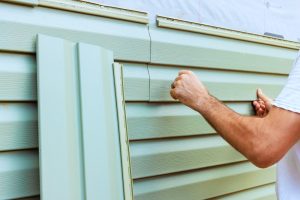 Worker carefully attaches green siding panels to house, focusing on precise fit for home renovation project.